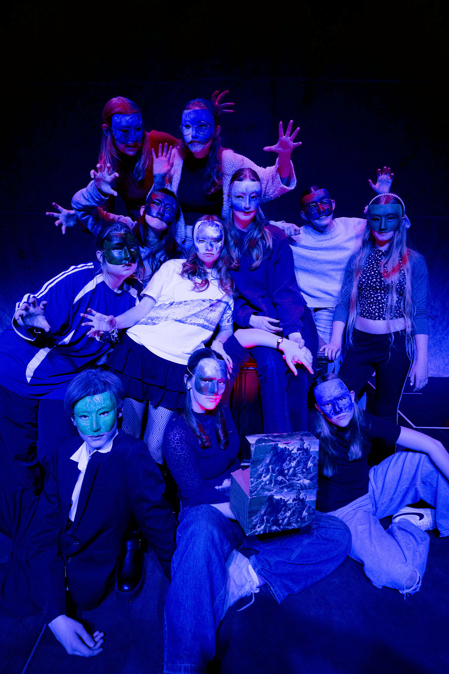 Gruppenbild des Jugendclubs in blauem Scheinwerferlicht, alle tragen bunte Halbmasken.